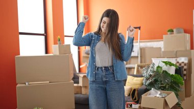 Genç, güzel, İspanyol bir kadın yeni evinde kendine gülerek duruyor.