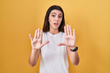 Sarı arka planda duran genç ve güzel bir kadın korku ifadesinden korkuyor ve dehşete düşmüş. El hareketlerini durdur, şok içinde bağır. panik konsepti. 