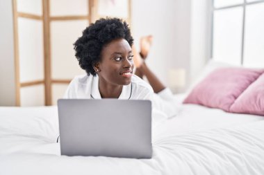 Young african american woman using laptop lying on bed at bedroom