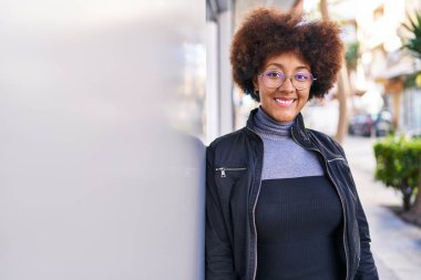 Afro-Amerikalı kadın gülümsüyor. Kendinden emin bir şekilde caddeye bakıyor.