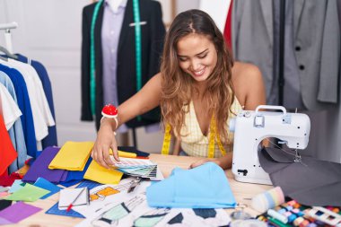 Young beautiful hispanic woman tailor looking color test and cloth at tailor shop