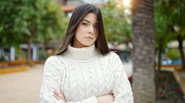 Parkta yüzü ve kolları çaprazlanmış bir şekilde duran güzel İspanyol bir kadın.