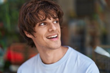 Sarışın genç adam gülümsüyor. Kendinden emin. Caddenin kenarına bakıyor.