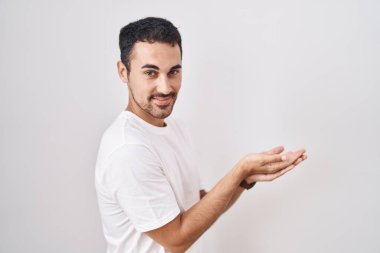 Beyaz arka planda duran yakışıklı İspanyol adam. Avuç içleri açık, fotokopi alanını gösteriyor. Gülümseyen mutlu bir gülümseme sunuyor. 