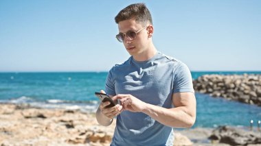 Genç İspanyol turist deniz kenarında rahat bir ifadeyle akıllı telefon kullanıyor.