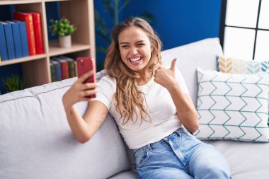 Genç İspanyol kadın akıllı telefonuyla video görüşmesi yapıyor. Parmağını kaldırıp gülümsüyor ve ağzını açıyor. 