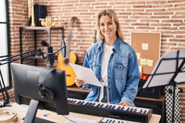 Young blonde woman musician playing piano keyboard at music studio