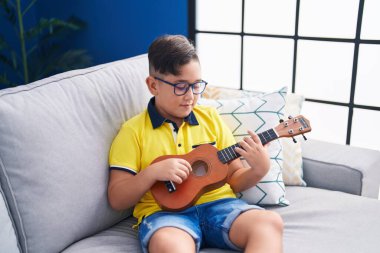 Evdeki kanepede oturmuş gitar çalan sevimli İspanyol çocuk.