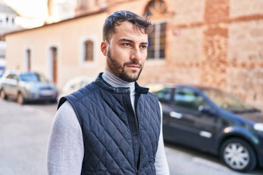 Young hispanic man with serious expression standing at street