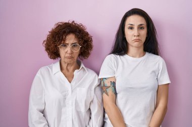 İspanyol anne ve kızı pembe arka plan üzerine günlük beyaz t-shirt giyiyorlar. Depresyondalar ve endişe içindeler. Kızgın ve korkmuş ağlıyorlar. hüzünlü ifade. 