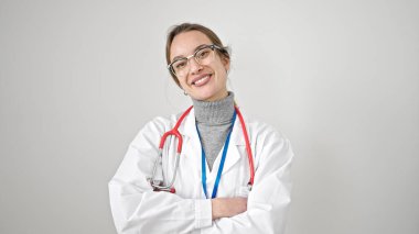 Beyaz arka planda kollarını kavuşturup gülümseyen genç beyaz kadın doktor.