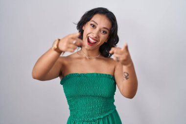 İzole edilmiş arka planda duran genç İspanyol kadın seni ve kamerayı işaret ediyor, mutlu ve mutlu gülümsüyor. 