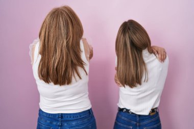 Hispanic mother and daughter wearing casual white t shirt over pink background hugging oneself happy and positive from backwards. self love and self care 