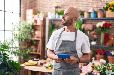 Young bald man florist smiling confident using touchpad at florist