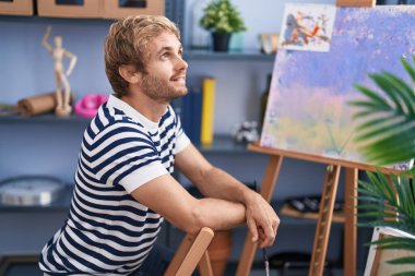 Sanat stüdyosunda kendine güvenen genç bir sanatçı oturuyor.