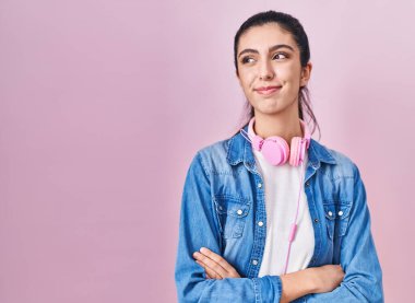 Young beautiful woman standing over pink background smiling looking to the side and staring away thinking. 