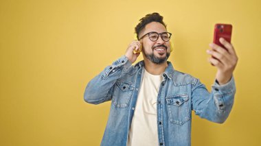 İzole edilmiş sarı arka planda dans eden genç latin adam müzik dinliyor.