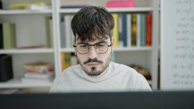 Genç İspanyol erkek üniversite öğretmeni üniversite sınıfında bilgisayar kullanıyor.