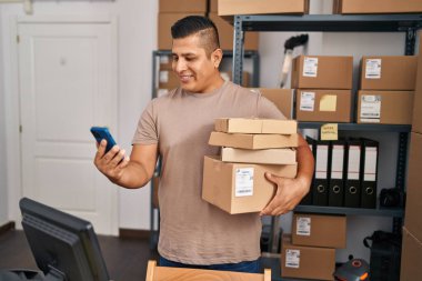 Genç latin adam ecommerce iş işçisi Ofiste akıllı telefon paketlerini tutuyor