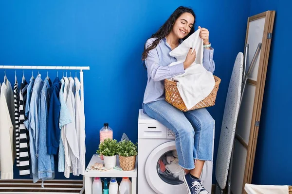 Genç İspanyol kadın çamaşırhanede yüzlerine sotf kıyafetlerle dokunuyor.