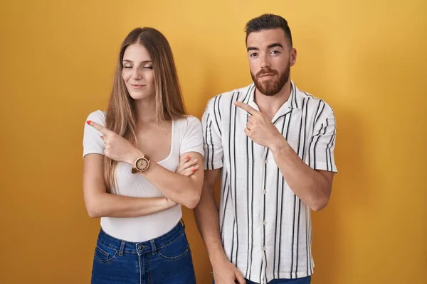 Sarı Arka Planda Duran Genç Bir Çift Ile Işaret Ederek — Stok fotoğraf