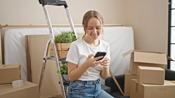 若いですブロンド女性使用してスマートフォン座っている上のはしごで新しい家 — ストック写真