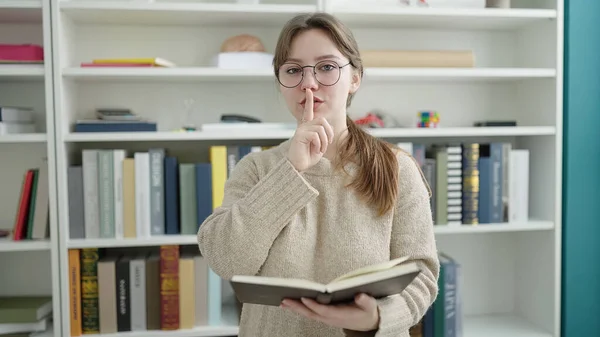 Young Blonde Woman Student Reading Book Doing Silence Gesture Library — Stock Fotó