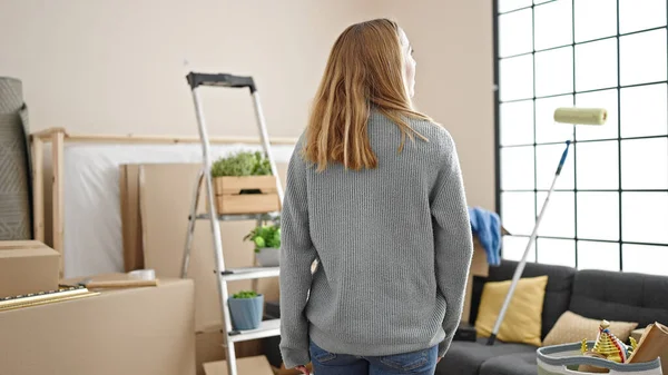 Sarışın genç kadın yeni evinde arka planda duruyor.