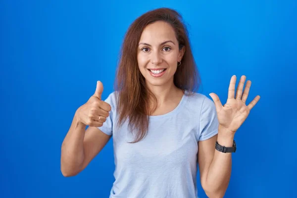 布鲁内特女人站在蓝色的背景上 用六号手指指指指点点 自信而快乐地微笑着 — 图库照片