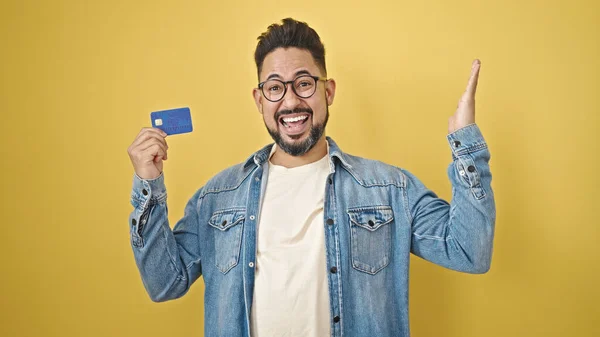 stock image Young latin man holding credit card with winner gesture over isolated yellow background