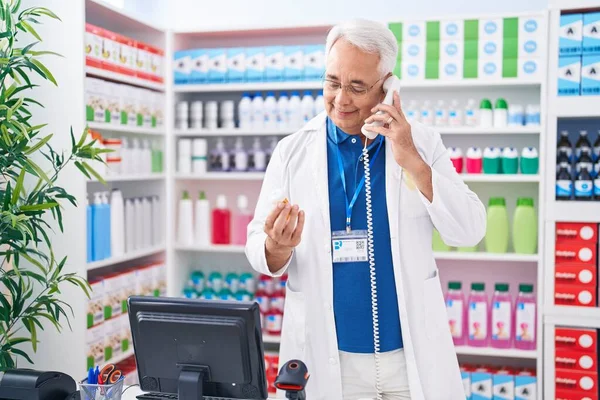 中年白发男子药剂师在药店打电话 手里拿着药瓶 — 图库照片