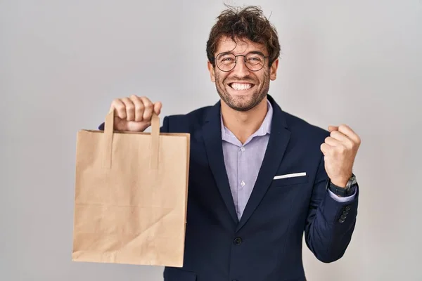 stock image Hispanic business man holding delivery bag screaming proud, celebrating victory and success very excited with raised arms 