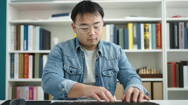 Young chinese man student using computer studying at library university
