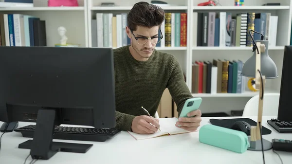 Young Hispanic Man Student Using Smartphone Writing Notebook Library University — Stock fotografie