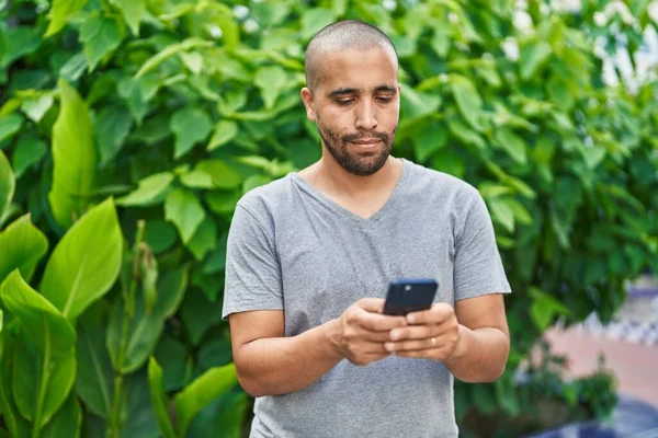 年轻的拉丁裔男子在公园里用带有严肃表情的智能手机 — 图库照片