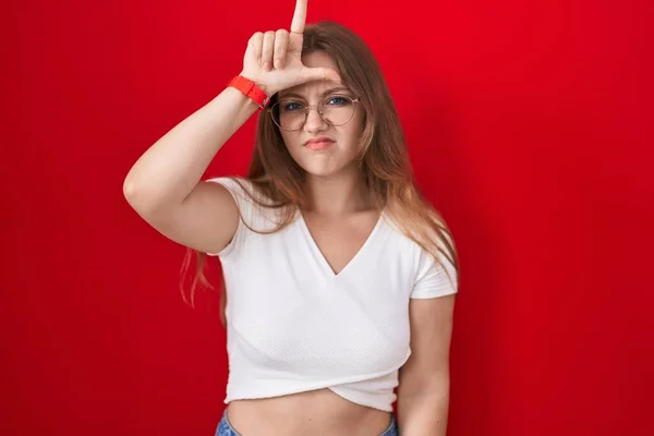 Mladá Běloška Stojí Nad Červeným Pozadím Dělá Legraci Lidí Prsty — Stock fotografie