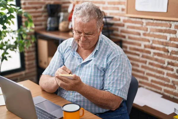 オフィスのメモ用紙にノートパソコンを使っている中年の白髪のサラリーマン — ストック写真