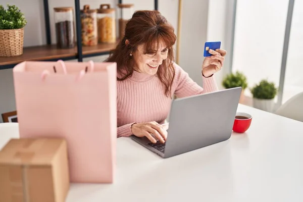 中年妇女坐在家里桌子上 用信用卡和笔记本电脑购物 — 图库照片