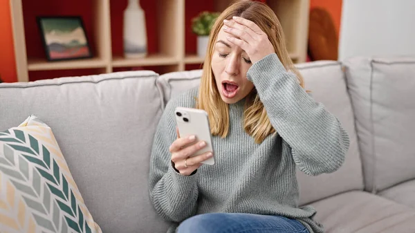 Young Blonde Woman Using Smartphone Sitting Sofa Surprise Expression Home — Stock Photo, Image