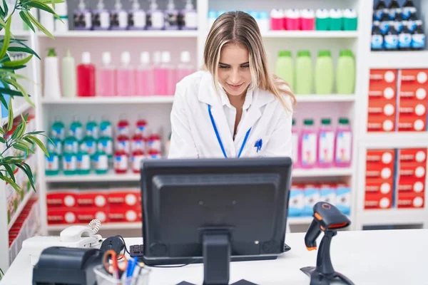 年轻的金发女药剂师带着自信的笑容在药店使用电脑 — 图库照片