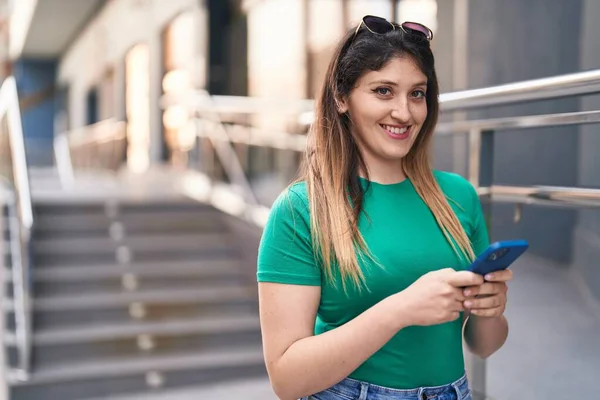 若いヒスパニック系の女性が自信を持って笑顔でスマートフォンを使って通り — ストック写真