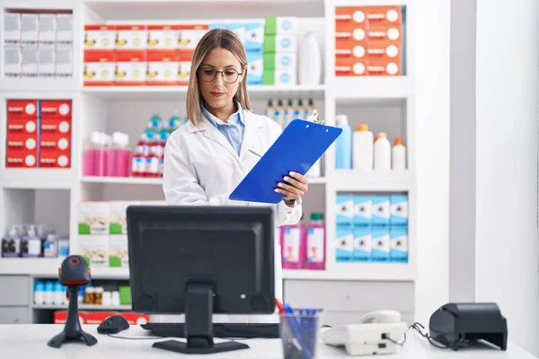 Young Beautiful Hispanic Woman Pharmacist Reading Document Using Computer Pharmacy — 스톡 사진