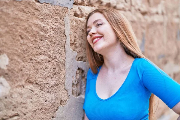 年轻的红头发女人面带微笑 自信地看着旁边孤立的砖墙背景 — 图库照片