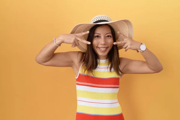 中世中国の女性は黄色の背景の上に夏の帽子を身に着けています顔の上に指で平和のシンボルを行います 笑顔明るい勝利を示す — ストック写真