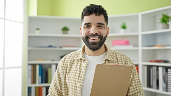 Young Hispanic Man Student Smiling Confident Holding Clipboard Library University — ストック写真