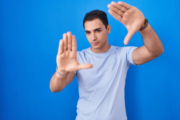 Young Hispanic Man Standing Blue Background Doing Frame Using Hands — Foto Stock