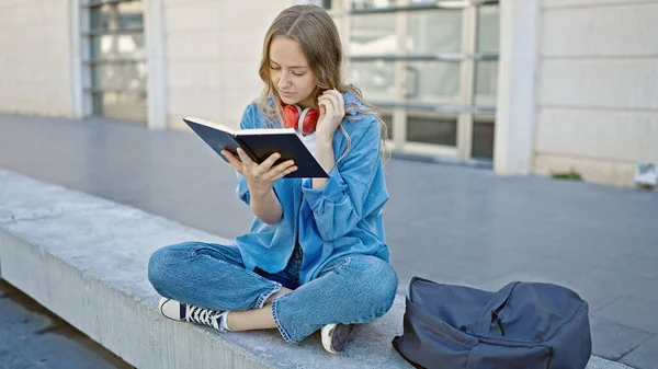 大学时 年轻的金发女学生坐在长椅上看书 — 图库照片
