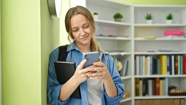 Junge Blonde Studentin Nutzt Smartphone Mit Buch Der Bibliothek — Stockfoto