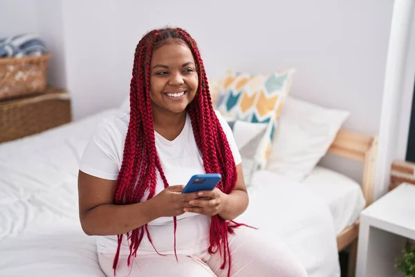 Afroamerykanka Pomocą Smartfona Siedzi Łóżku Sypialni — Zdjęcie stockowe
