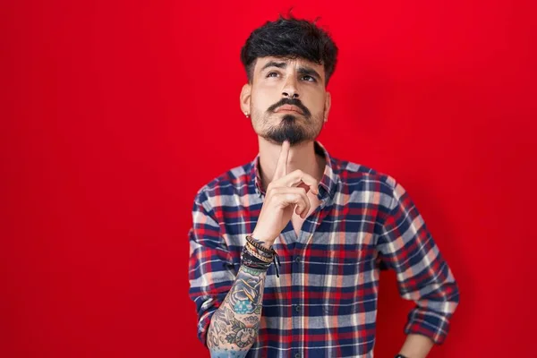 Ung Latinamerikansk Man Med Skägg Står Över Röd Bakgrund Tänker — Stockfoto